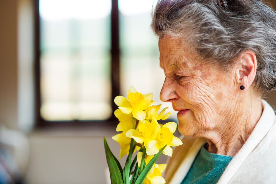 A senior woman smells a bouquet of yellow flowers.
