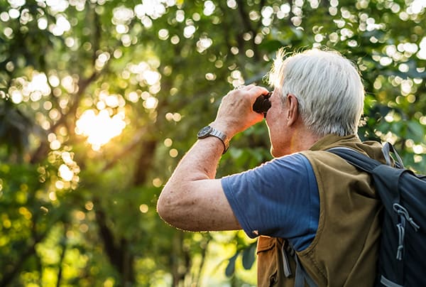A senior man looking through binoculars during a sunset