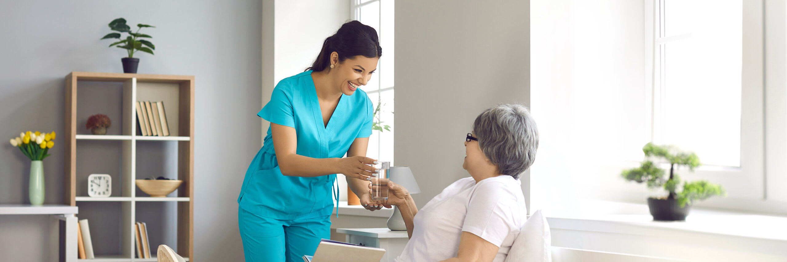 An in-home caregiver handing a glass of water to a senior