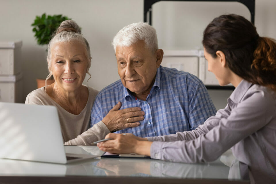 A senior couple looks at a laptop while a younger woman talks with them