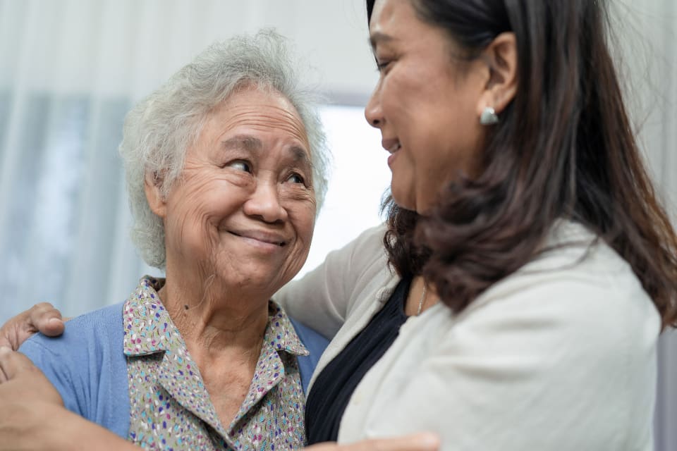 A caregiver and senior woman with dementia embrace.
