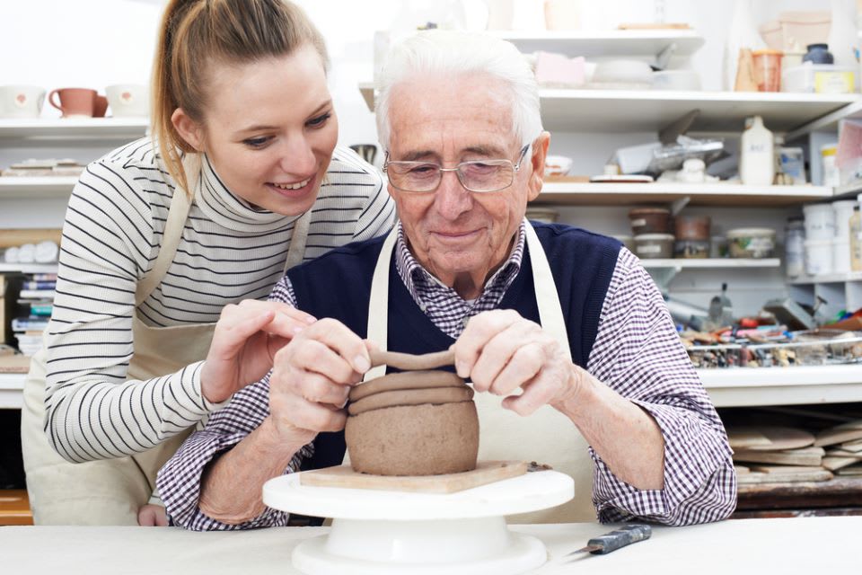 Young woman helping an elderly man make a clay pot.